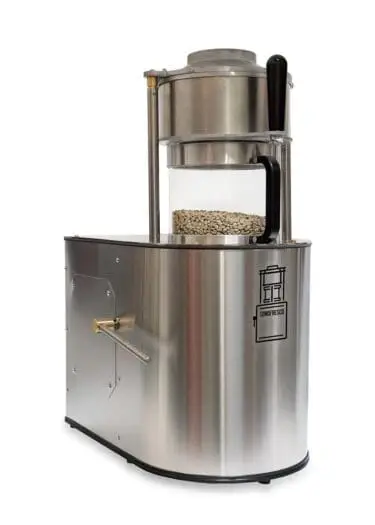 Stainless steel Sonofresco two-pound coffee roaster with a transparent roasting chamber containing unroasted green coffee beans.