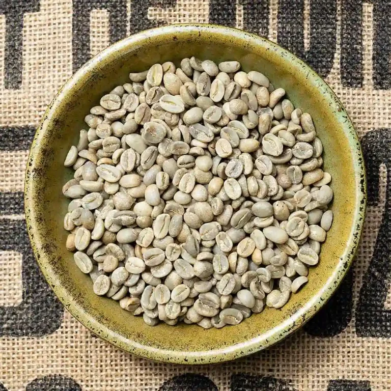 Top-down view of a green ceramic bowl filled with unroasted green coffee beans on a burlap surface with printed text.