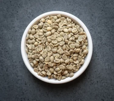 Bowl of Kenya AA green coffee beans on a dark surface